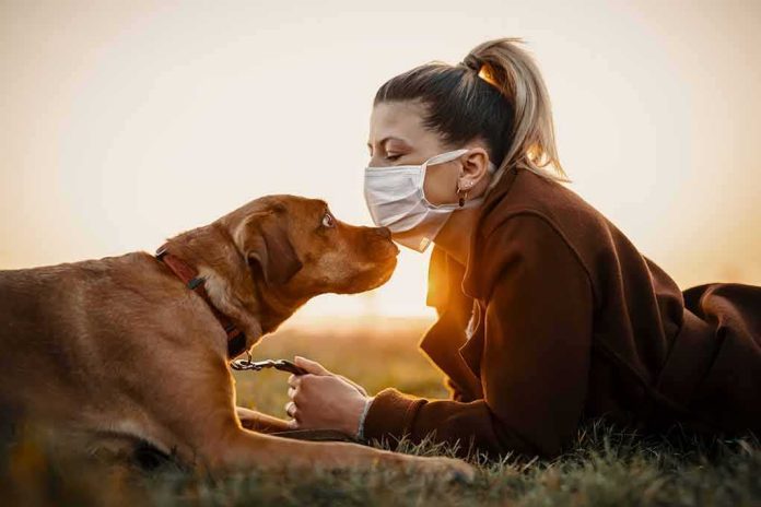 Woman in mask touching noses with brown dog at sunset