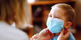 child wearing a surgical mask being adjusted by an adult