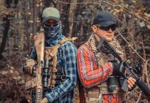 Two armed individuals in tactical gear standing back to back in a forest