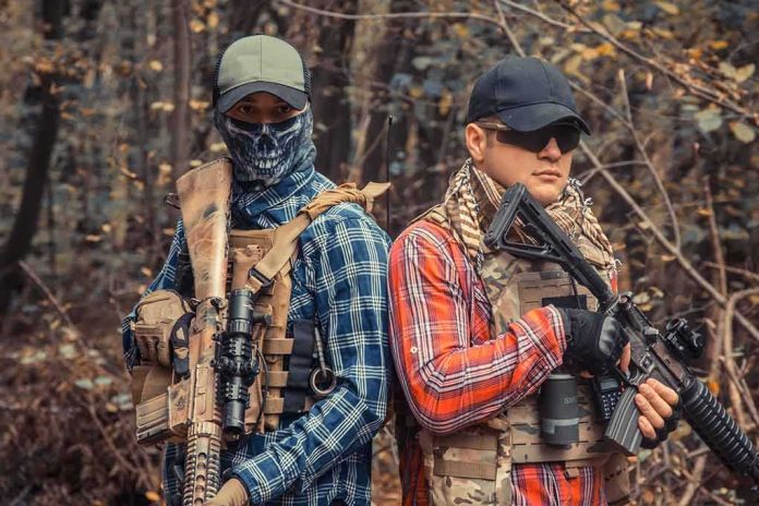 shutterstock_1691717854 Two armed individuals in tactical gear standing back to back in a forest
