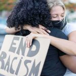 Two people hugging at a protest holding a cardboard sign