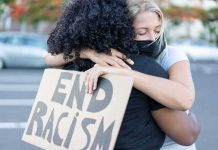 Two people hugging at a protest holding a cardboard sign