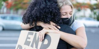 Two people hugging at a protest holding a cardboard sign