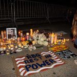 Activist Label Sparks Outrage — Was It Murder? Vigil with candles and signs on a sidewalk at night