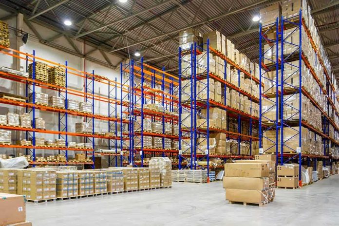 shutterstock_1929800966 Warehouse aisles with tall blue and orange pallet racks filled with boxes