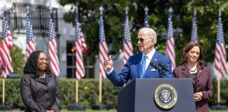 Joe Biden speaking at a podium outdoors with Kamala Harris standing nearby