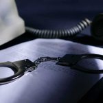 Handcuffs on a document beside a coiled telephone handset