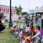 Police officer kneels at a memorial with flowers and crosses