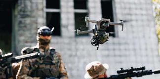 Quadcopter drone flying above soldiers in camouflage