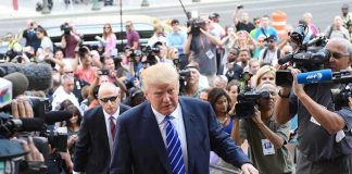 Donald Trump walks up steps through a crowd as A. J. Calloway films nearby