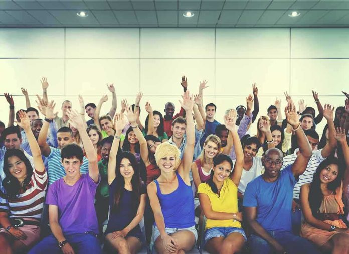 shutterstock_325412837 Group of people raising hands in an indoor audience
