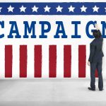 El-Sayed Accused of Taking ‘Terrorist’ Money Man in suit writing on large campaign banner with stars and stripes