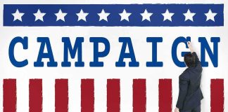 Man in suit writing on large campaign banner with stars and stripes
