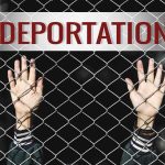 Hands gripping chain-link fence with deportation sign