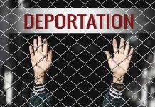 Hands gripping chain-link fence with deportation sign