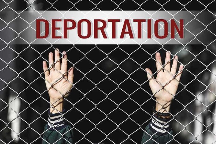 Hands gripping chain-link fence with deportation sign
