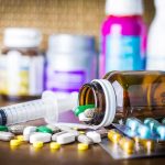 Trans Tribunal Smacks Doctor — $28K Over One Shot Medicine pills and syringe on table with brown bottle