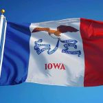 Iowans Wreck Dem Senate Nominee for Loving Taxes Iowa state flag waving on a flagpole against a clear blue sky