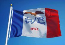 Iowa state flag waving on a flagpole against a clear blue sky