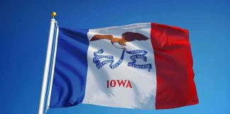 Iowans Wreck Dem Senate Nominee for Loving Taxes Iowa state flag waving on a flagpole against a clear blue sky