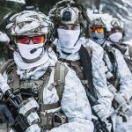 Soldiers in white winter camouflage gear standing in a snowy forest