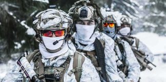Soldiers in white winter camouflage gear standing in a snowy forest