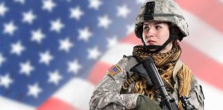 Soldier in camouflage holding a rifle against a blurred American flag