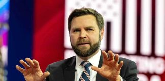 Man in suit speaking on stage with hands raised