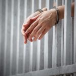 Couple Convicted in $13M Aid RIPOFF handcuffed hands resting through prison bars