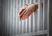 handcuffed hands resting through prison bars