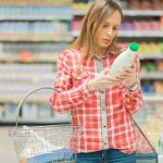 Woman reading a bottle label in a grocery store aisle