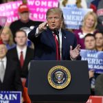 Donald Trump speaking at a rally podium, pointing toward the audience