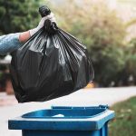 Feds Reportedly Grabbed Ilhan Omar’s TRASH gloved hand holding a black trash bag over a blue garbage bin