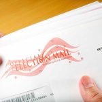 Election Offices Hit With Mystery White Powder A hand holding an envelope labeled Official Election Mail
