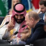 Mohammad bin Salman gestures while speaking with Vladimir Putin at a conference table