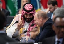 Mohammad bin Salman gestures while speaking with Vladimir Putin at a conference table