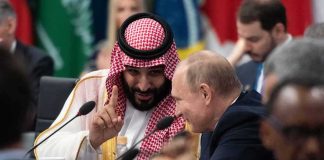 Mohammad bin Salman gestures while speaking with Vladimir Putin at a conference table