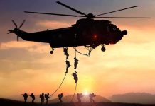 military helicopter with soldiers fast-roping at sunset