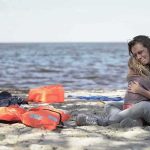 Woman hugging a child on a beach near discarded life jackets