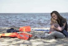 Woman hugging a child on a beach near discarded life jackets