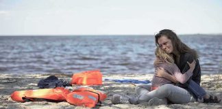 Woman hugging a child on a beach near discarded life jackets