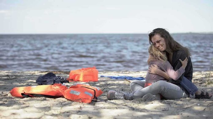 Woman hugging a child on a beach near discarded life jackets