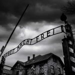 Entrance gate with wrought-iron sign at a historic brick complex under stormy skies