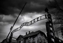 Entrance gate with wrought-iron sign at a historic brick complex under stormy skies
