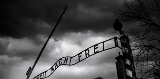 Entrance gate with wrought-iron sign at a historic brick complex under stormy skies