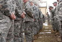 Soldiers in camouflage uniforms stand in two facing rows outdoors