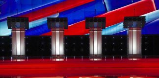 Democrat SNAPS at Susan Collins Mid-Debate Debate stage with four empty podiums and bright red and blue backdrop