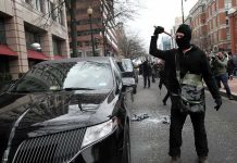 Masked protester raises tool to strike black car on city street